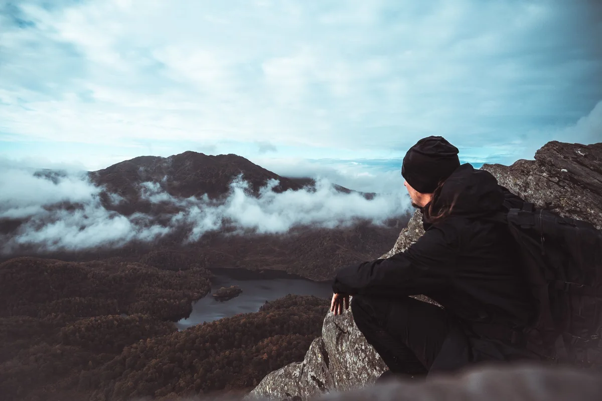 Eine Person sitzt über einer wolkenverhangenen Berglandschaft